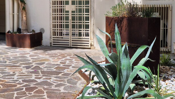 A courtyard with stone flooring, a metal gate, and potted plants.