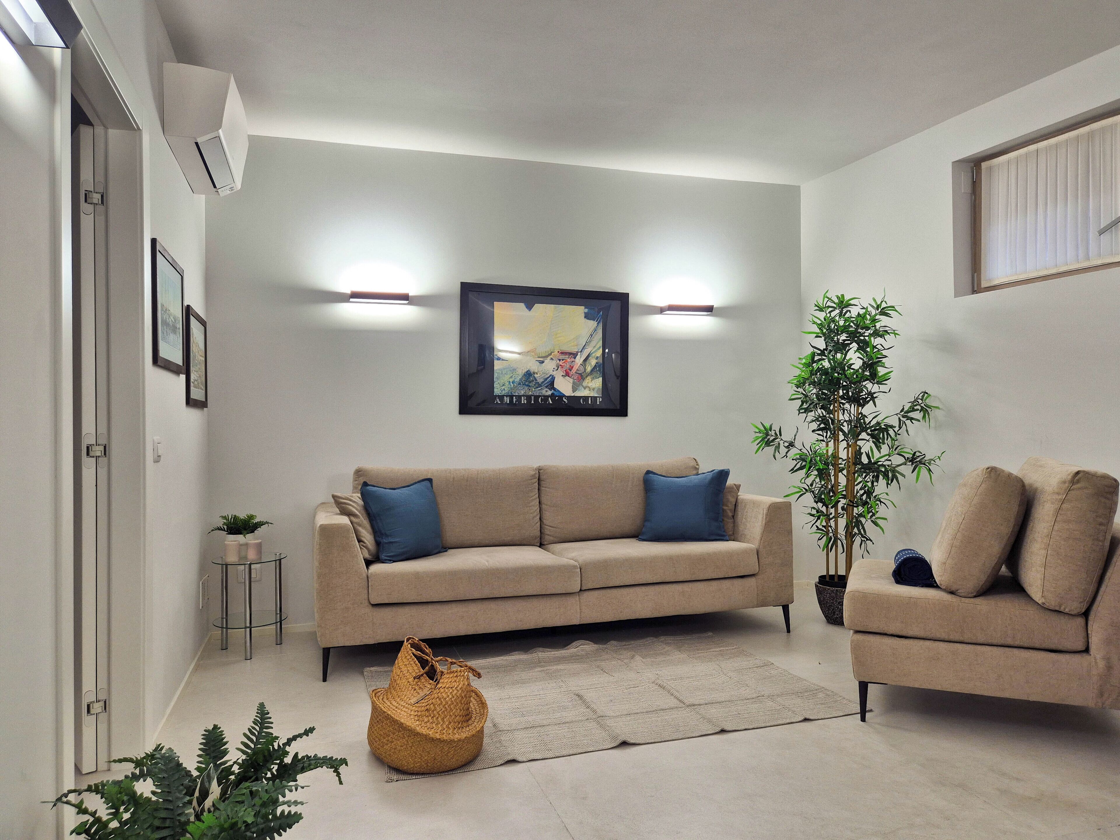 A living room with a beige sofa, a blue cushion, a woven basket, and a large potted plant.