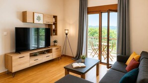 A modern living room with a TV, wooden cabinet, floor lamp, and a balcony with outdoor furniture. - Alimos Cozy Getaway, close to the beach (Alimos)