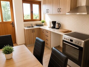 A modern kitchen with wooden cabinets, a built-in oven, a stove, a sink, and a window with a view of trees.