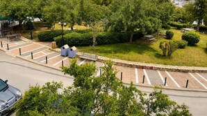 A parking area with a stone wall, trees, and a view of a modern building with a balcony. - Alimos Cozy Getaway, close to the beach (Alimos)
