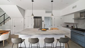 Une cuisine moderne dotée d’un îlot central, de tabourets de bar et d’un coin repas avec une table et des chaises en bois.