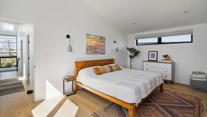 Une chambre à coucher moderne avec un lit en bois, une grande fenêtre, un tableau et une vue sur l’extérieur.