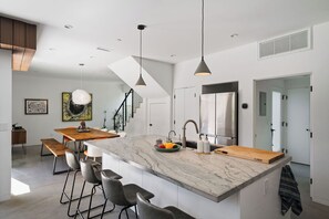 Una cocina moderna con encimera de mármol, taburetes de bar, luces colgantes y una isla grande.