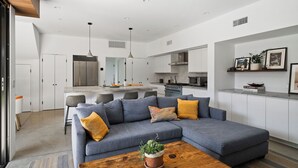 Un salon moderne avec un canapé d’angle gris, une table basse en bois et une cuisine en arrière-plan.