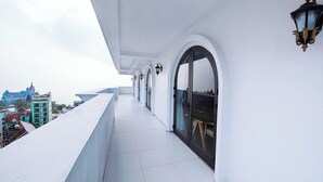 A balcony with white tiled flooring, a black table with chairs, and a view of a building in the background. - Celina Hotel - Khach San Tam Dao (Tam Dao)