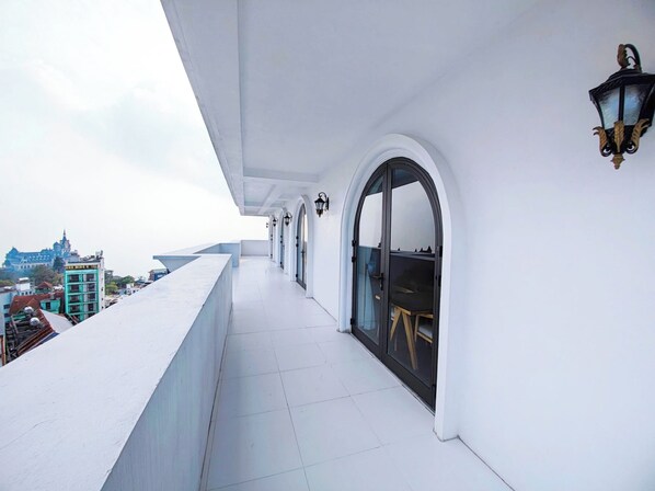 A balcony with white tiled flooring, a black table with chairs, and a view of a building in the background. - Celina Hotel - Khach San Tam Dao (Tam Dao)