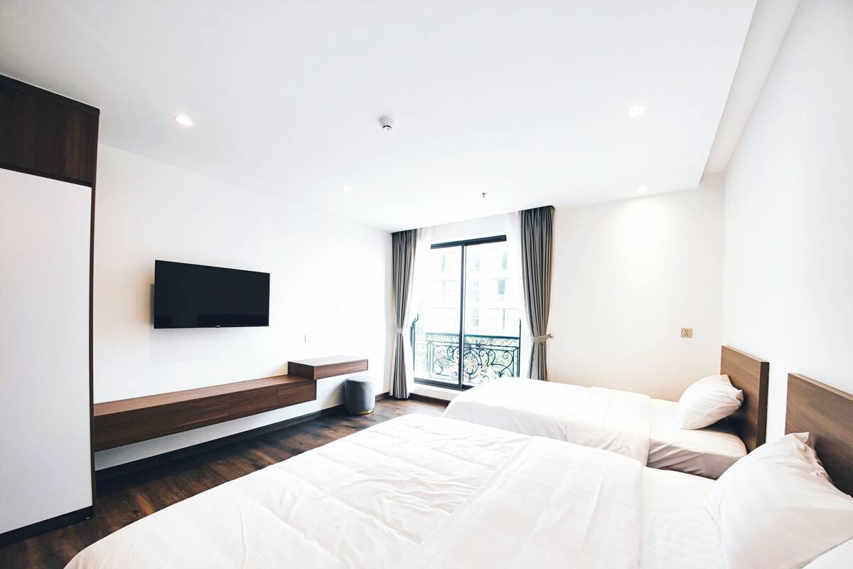 Une chambre d’hôtel moderne avec deux lits, un téléviseur à écran plat fixé au mur et un balcon avec des rideaux.