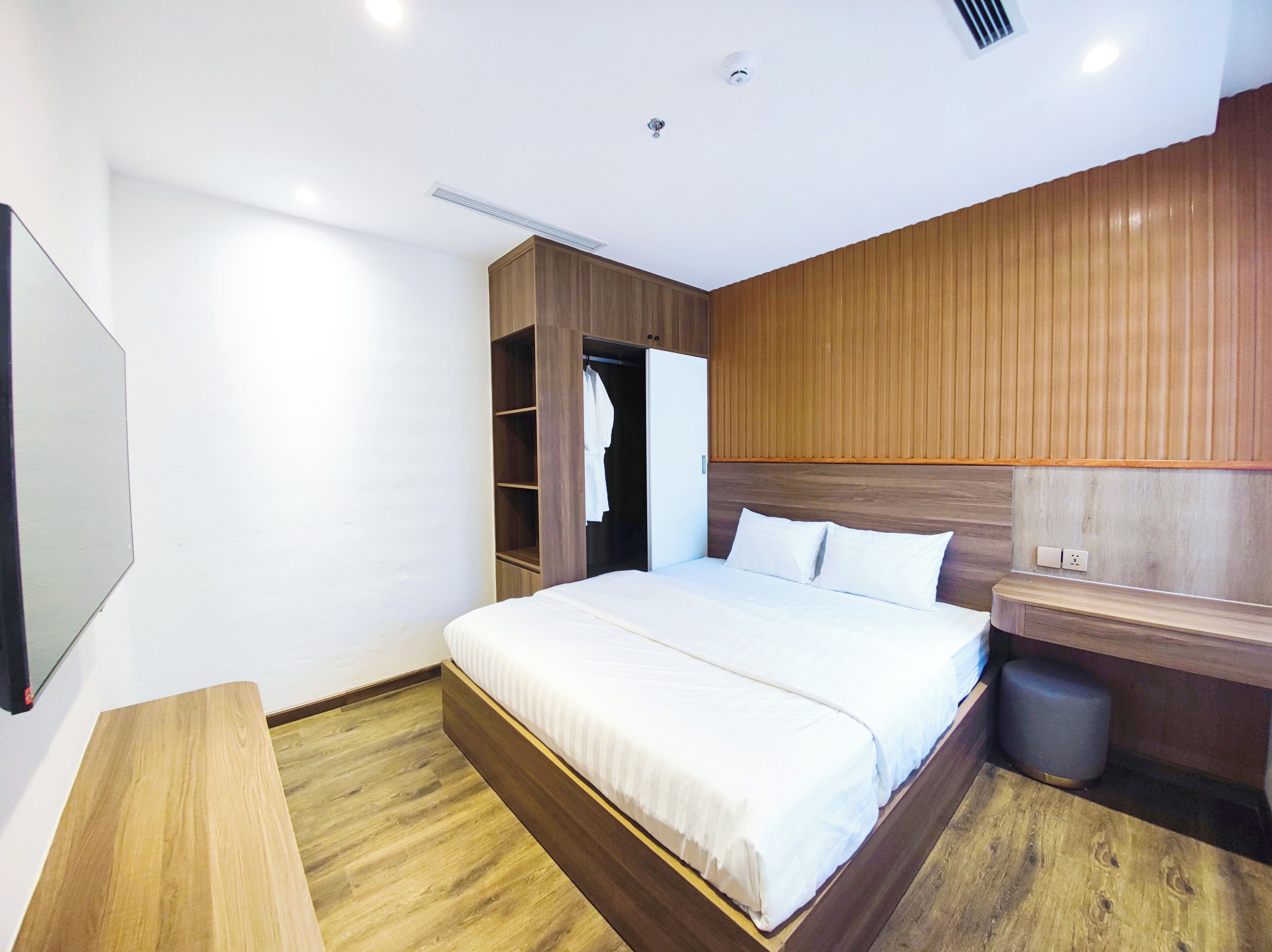 A modern bedroom with a wooden headboard, a bed with white linens, a wooden bench, and a built-in wardrobe.
