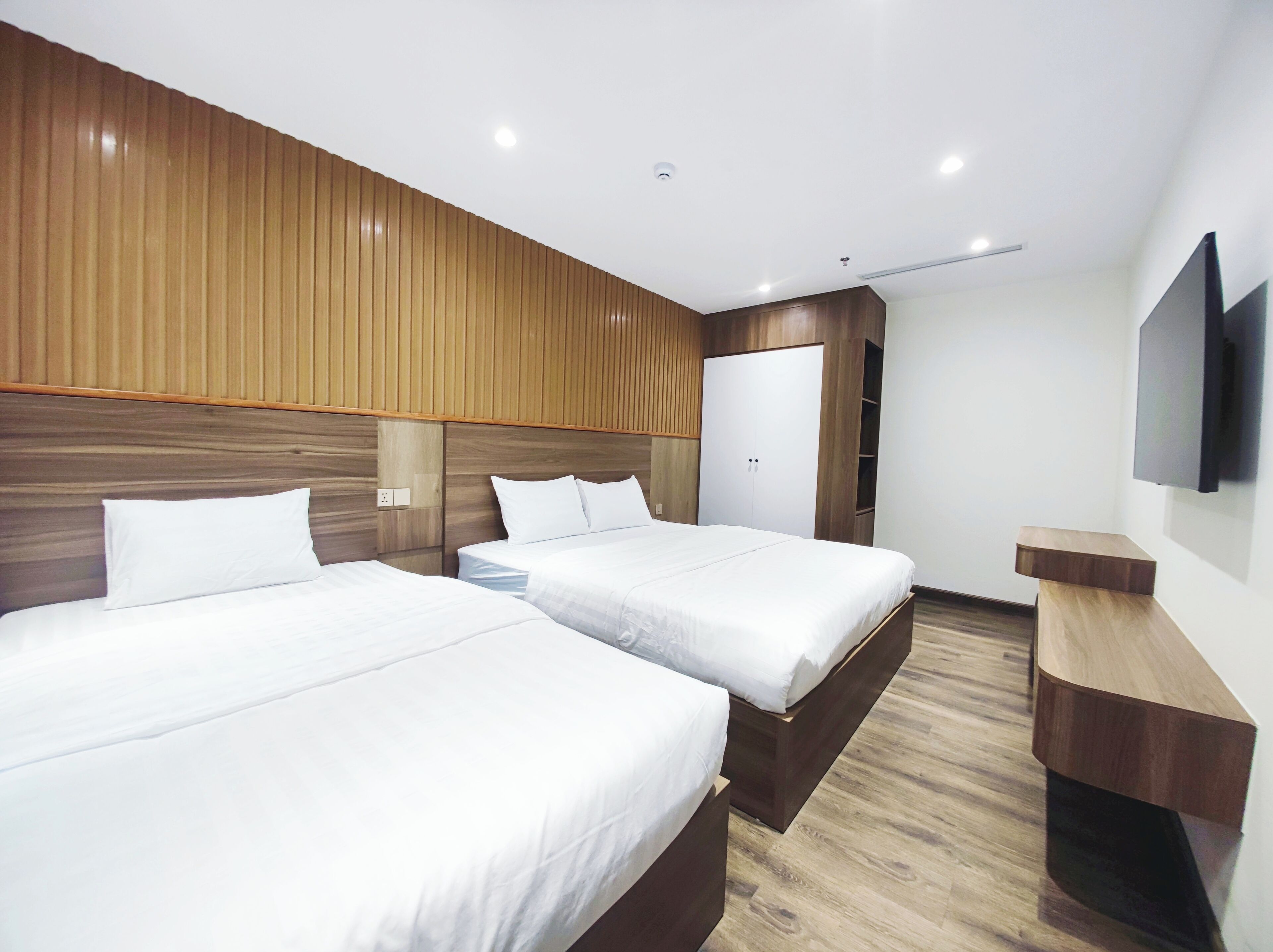 Ein Hotelzimmer mit zwei Betten, Holzvertäfelung an den Wänden, einem wandmontierten Flachbildfernseher und einem Nachttisch aus Holz.