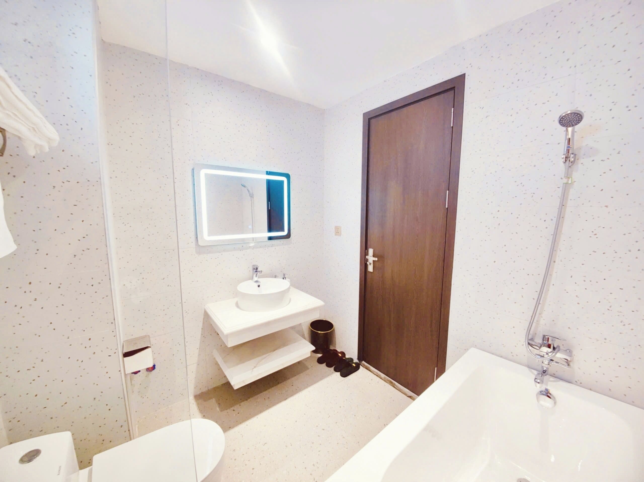 A modern bathroom with a white sink, a mirror with LED lighting, a shower, and a toilet.
