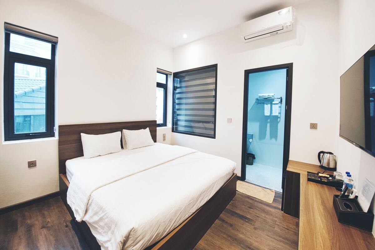 Une chambre d’hôtel moderne dotée d’un grand lit, d’une télévision à écran plat, d’un petit bureau et d’une salle de bain avec une porte en verre.