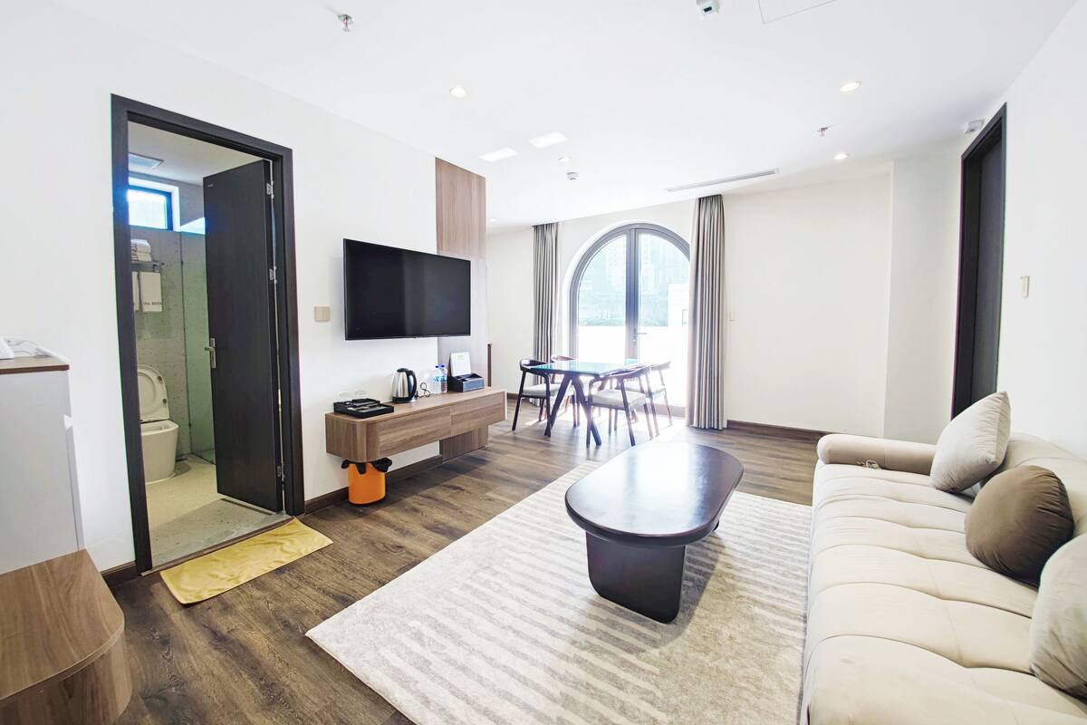 Une chambre d’hôtel moderne comprenant un coin salon, une table à manger, un canapé, un téléviseur à écran plat et une salle de bain avec des toilettes et une douche.