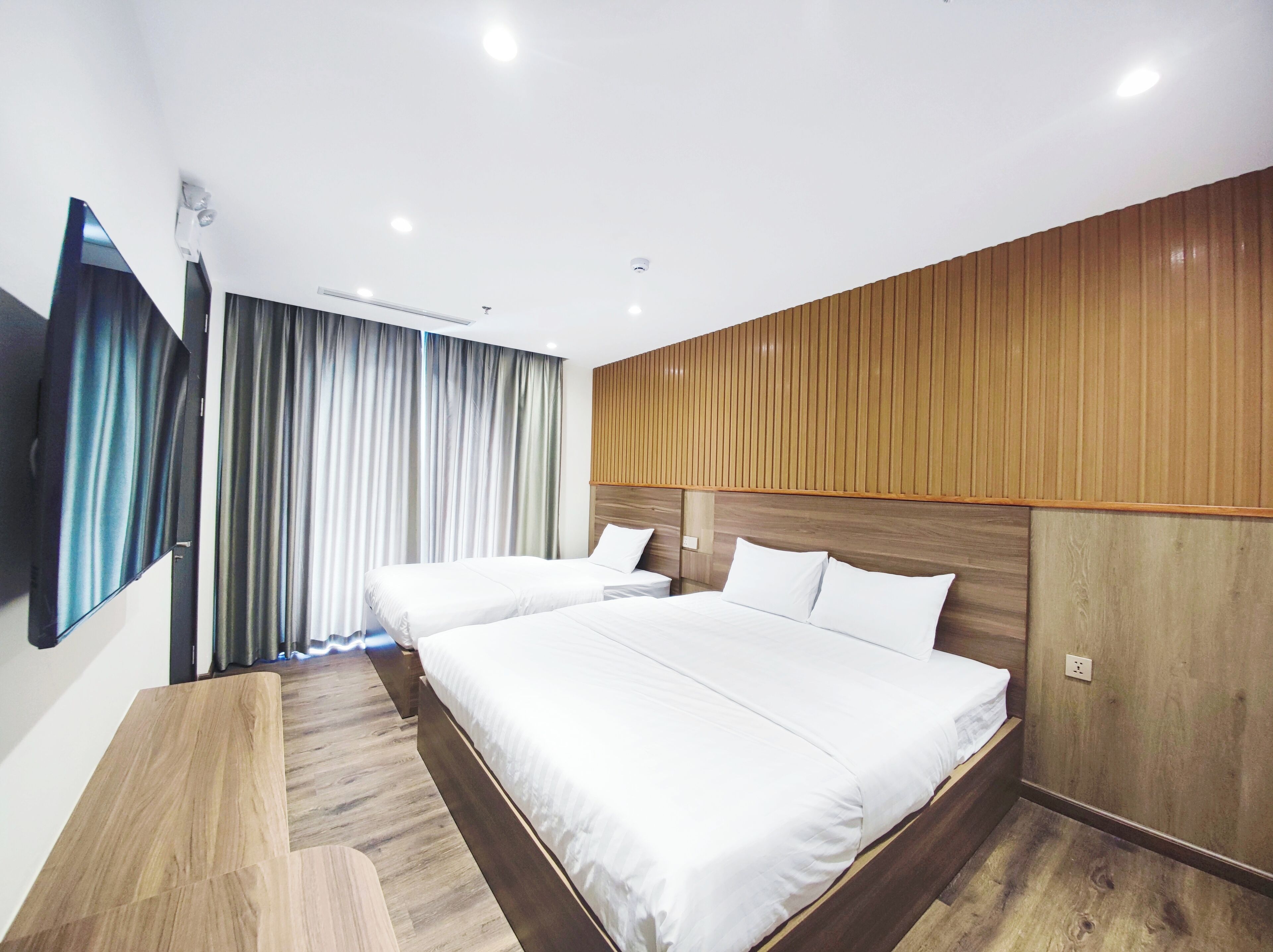 Una habitación de hotel moderna con dos camas, paneles de madera en las paredes, un espejo grande y un televisor de pantalla plana.