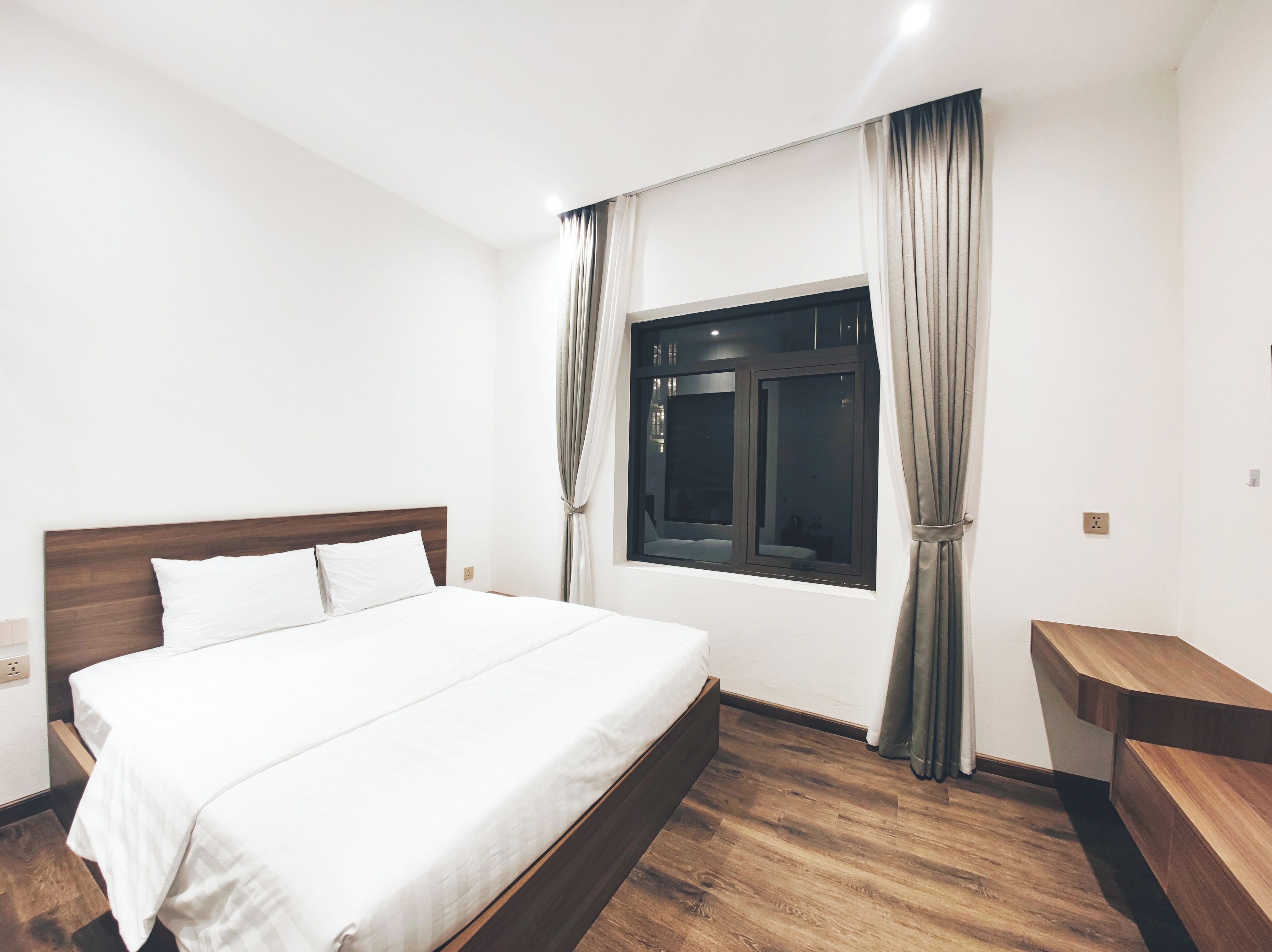 A modern hotel room with a large bed, wooden headboard, and a window with curtains.