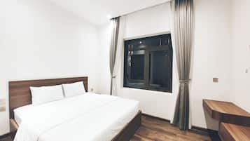 A modern hotel room with a large bed, wooden headboard, and a window with curtains.