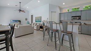 A spacious living area with a dining table, chairs, a sofa, and a kitchen with grey cabinets and a microwave.