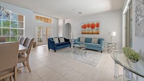 A spacious living room with a dining area, a blue sofa, and a glass coffee table.