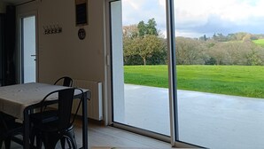 A room with a table, chairs, and a view of a green field through large windows. - Ty bugale in the heart of nature, 30 minutes from Lorient and its coast, ideal for recharging your batteries. (Inguiniel)