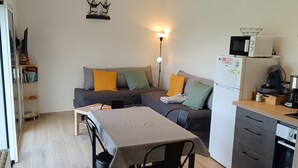 A compact living space with a kitchenette, a dining area, and a sofa with cushions. - Ty bugale in the heart of nature, 30 minutes from Lorient and its coast, ideal for recharging your batteries. (Inguiniel)
