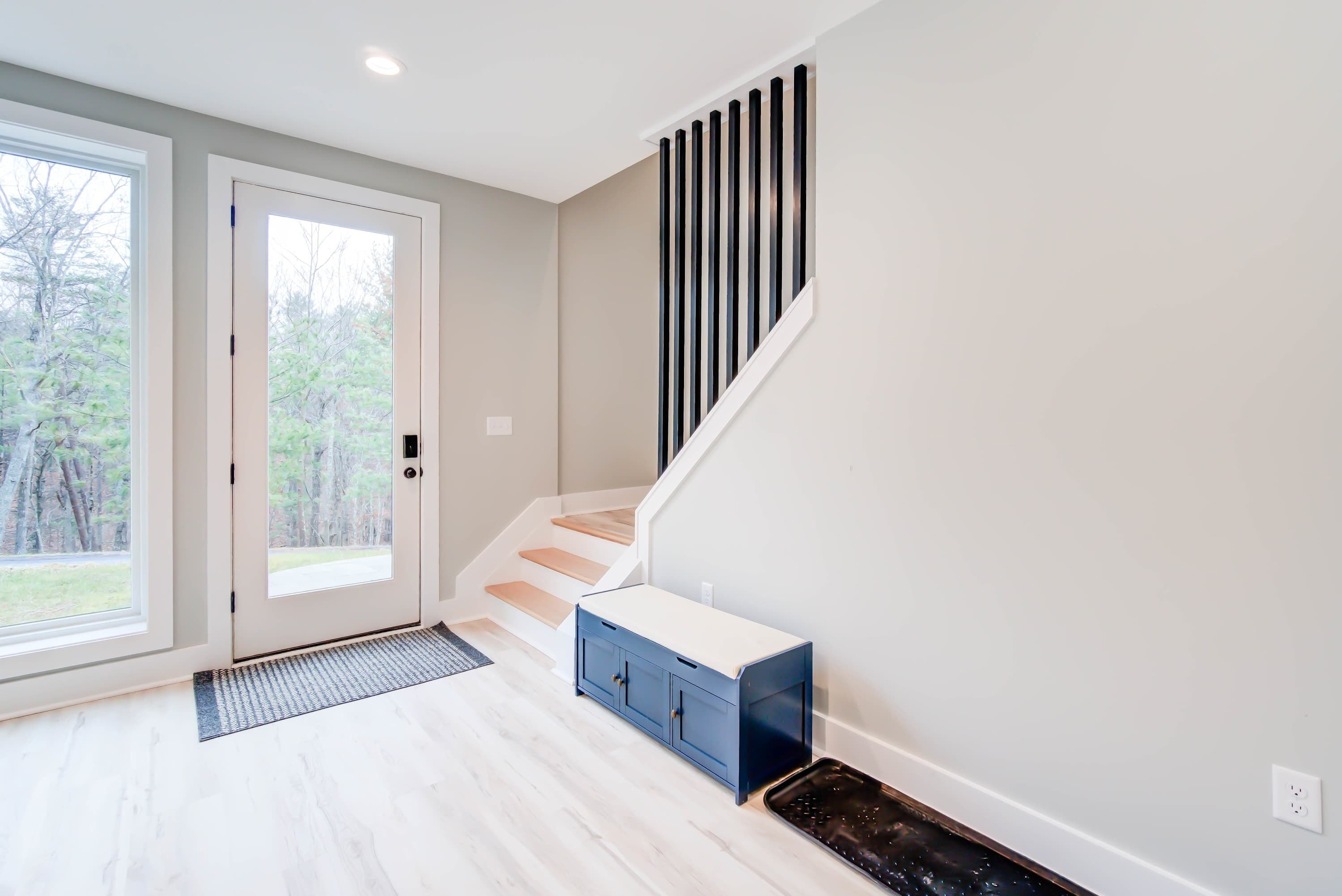 Un intérieur moderne avec un escalier, une porte donnant sur l’extérieur et un petit meuble bleu.