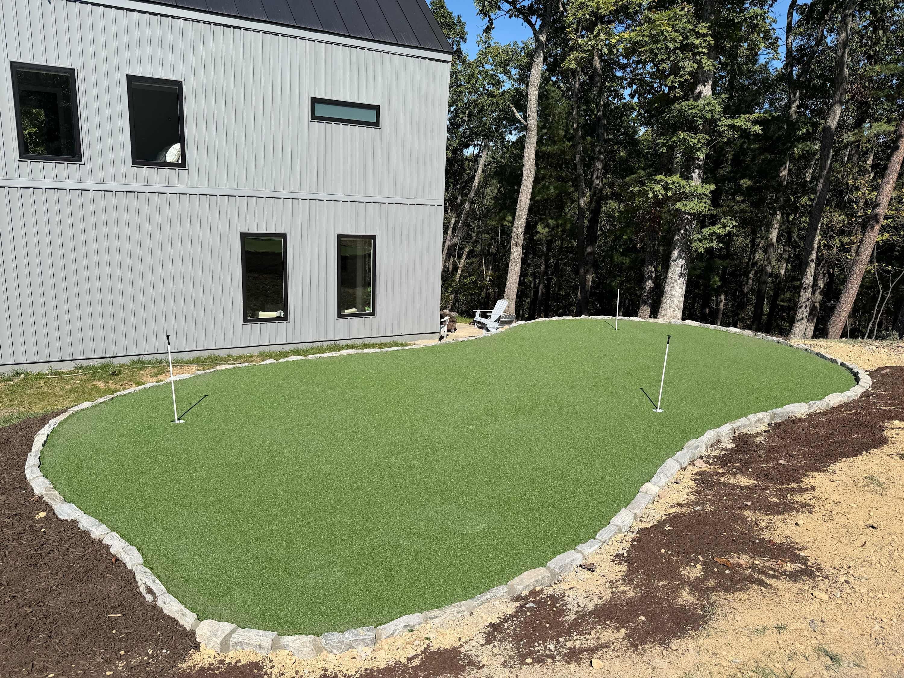 En modern byggnad med ett platt tak och stora fönster, omgiven av en välskött gräsmatta med en puttinggreen.