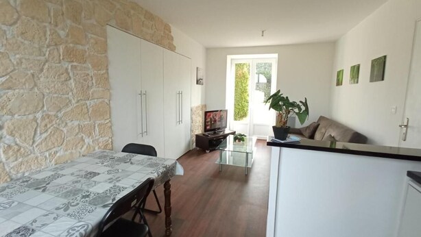 A modern kitchen with a stone wall, a dining table with chairs, a TV, and a sofa. - LE P'TIT LOGEMENT DE LOR'PHEE (CHANTEPIE)