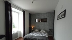 A bedroom with a bed, a window with curtains, a bedside table with a lamp, and a framed picture on the wall. - LE P'TIT LOGEMENT DE LOR'PHEE (CHANTEPIE)