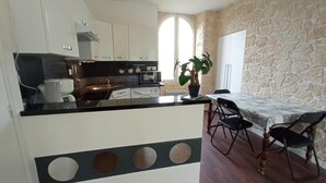 A compact kitchen with white cabinets, a black countertop, and a dining area with a table and chairs. - LE P'TIT LOGEMENT DE LOR'PHEE (CHANTEPIE)