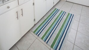 Eine Küche mit weißen Schränken, einer Edelstahl-Spüle, einer blauen Kaffeemaschine und einem Streifenmuster-Teppich.