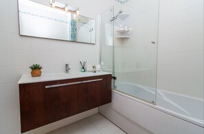 Un baño moderno con tocador de madera, un espejo grande y una ducha con cerramiento de vidrio.