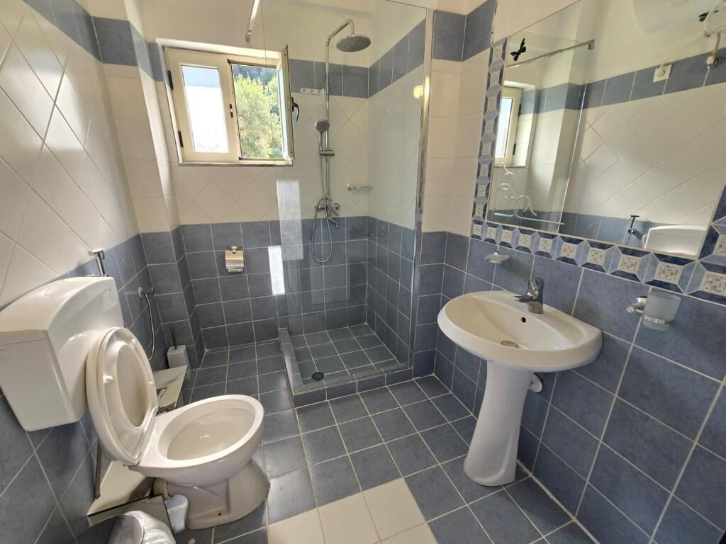 A bathroom with a toilet, sink, shower, and a window.