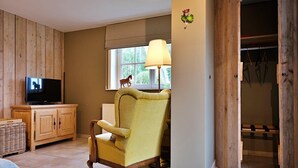 A room with a wooden paneled wall, a television on a wooden cabinet, a yellow armchair, a window with a view of trees, and a wooden wardrobe. - Ter Polders (Damme)