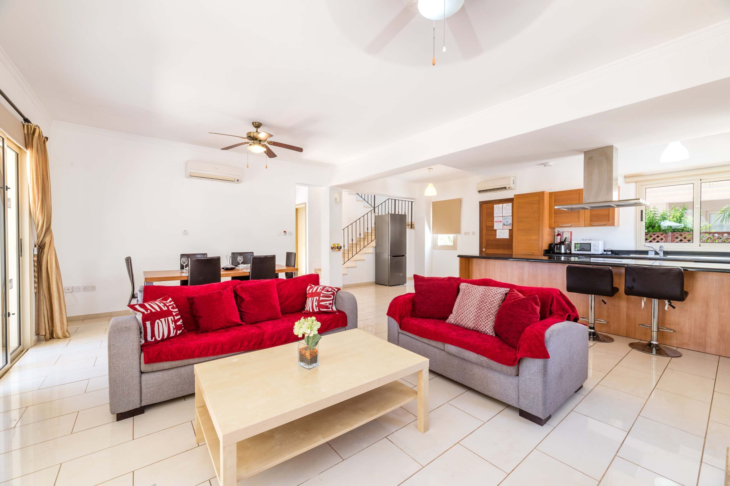 A spacious living area with two grey sofas and red cushions, a wooden coffee table, and a kitchen area with a modern design.