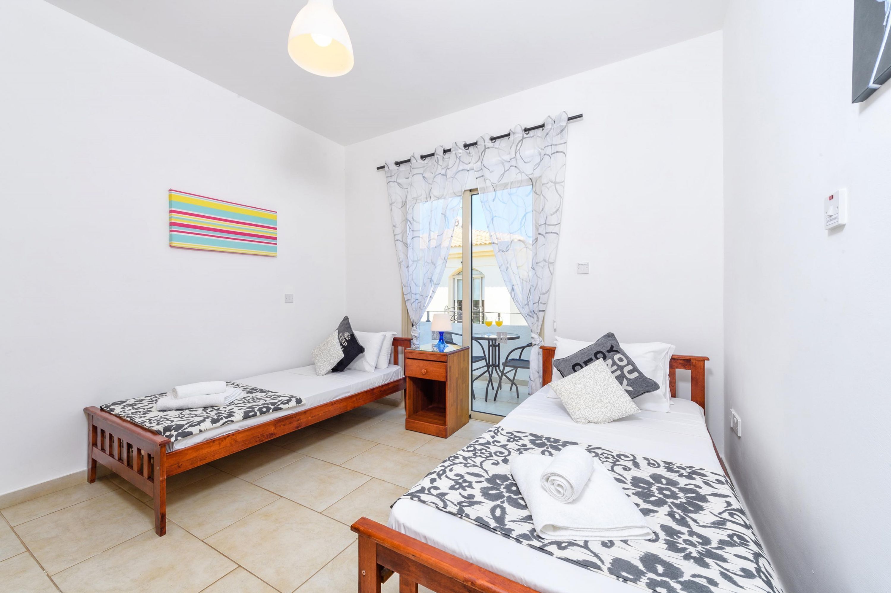 A room with two single beds, a small table, a chair, and a window with curtains.