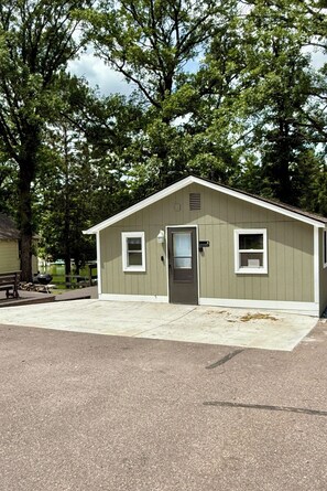 A small, single-story building with a door and two windows, surrounded by trees.