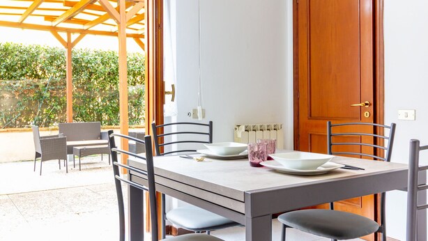 A dining area with a table set for four, chairs, a wooden pergola, and a door. - La Casa Di Nico by TuscanyWeGo (Capannori)