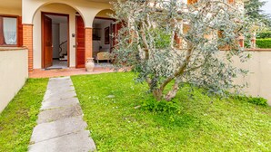 A courtyard with a pathway leading to a building with a brick facade and arched doorways. - La Casa Di Nico by TuscanyWeGo (Capannori)