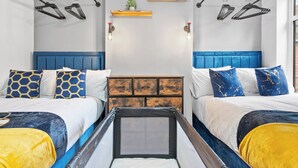 A hotel room with two beds, a blue headboard, a wooden nightstand, and wall-mounted lights.