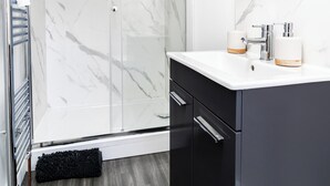 A modern bathroom with a glass shower enclosure, a white marble backsplash, and a black cabinet.