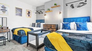 A modern bedroom with two beds, a desk, and a chair. There are wall-mounted shelves with plants and hooks for hanging items.
