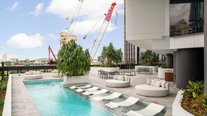 Un área de piscina en la azotea con una vista despejada del horizonte de la ciudad, incluyendo grúas de construcción.