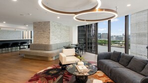 Un espacio lounge moderno con sofá, sillones, una mesa de centro y vistas de la ciudad a través de amplios ventanales.