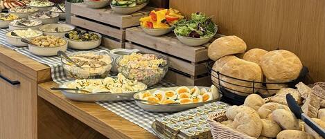 A buffet table with various food items including salads, meats, cheeses, and bread.