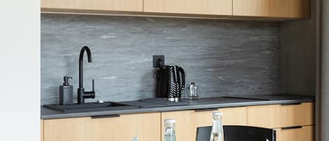 Una cocina moderna con armarios de madera, un grifo negro y una encimera negra. Hay una mesa redonda con platos, tazas y una botella.