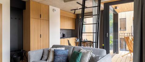 A modern loft apartment with a loft bed, a grey sofa, a wooden coffee table, and a large window.