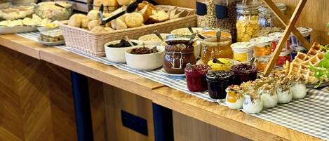 A buffet table with various food items including pastries, bread, and condiments.