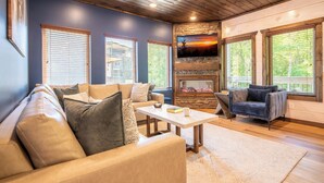 A cozy living room with a stone fireplace, leather sofas, and large windows. - *Stunning 4BD Lodge w/ POOL + Hot Tub + Near TOWN* (Pigeon Forge)