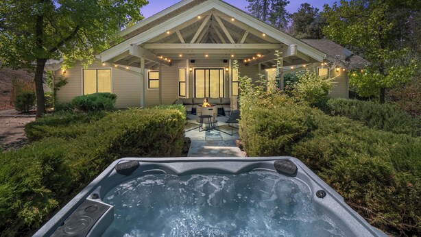 A house with a covered patio, a hot tub, and a well-maintained garden. - NEW - Fire pit - Game room - Sleeps 14 - 40 acres (Ahwahnee)