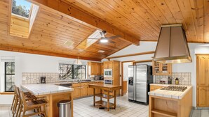 A spacious kitchen with wooden cabinets, a stainless steel refrigerator, and a large island with stools. - NEW - Fire pit - Game room - Sleeps 14 - 40 acres (Ahwahnee)